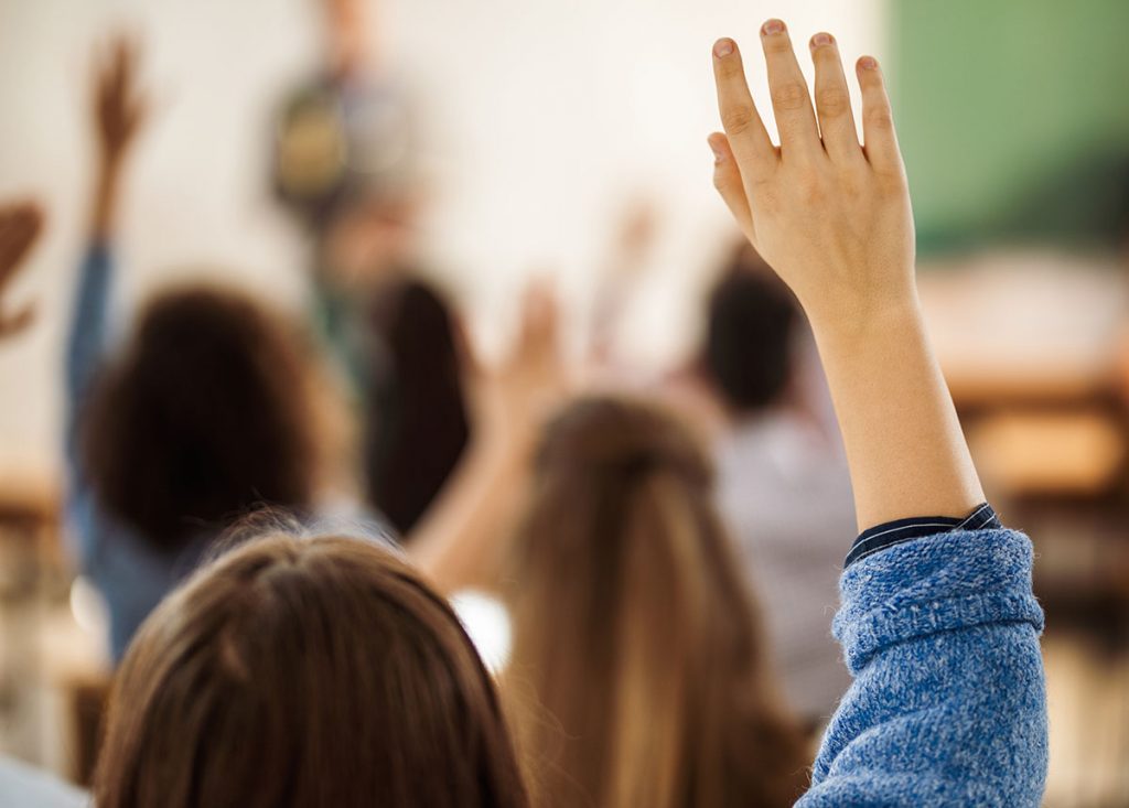 Back view of female student raising hand on a class.